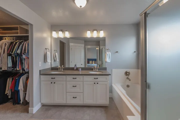 Dual vanity with undermount sinks, white cabinetry with dark hardware, and a solid-surface countertop