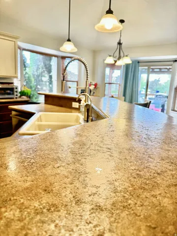 Kitchen featuring a dual-basin sink, gooseneck faucet, light-toned countertops, and pendant lighting