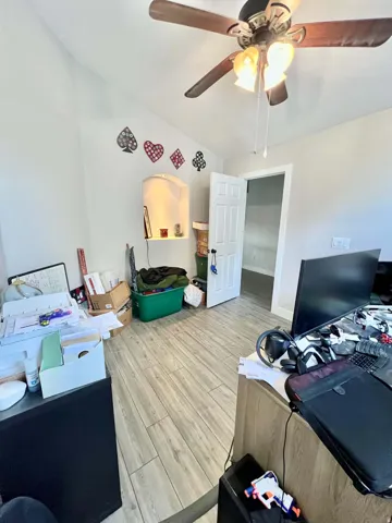 Wood-finish flooring, ceiling fan with integrated lighting, arched wall niche, and white interior door