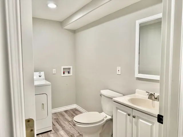 Recessed ceiling lighting, wood-finish flooring, white vanity with integrated sink, wall-mounted mirror, and laundry hookups