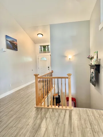 Wood-finish flooring throughout, light wood stair railing with decorative wrought iron spindles, a white paneled entry door with an arched glass insert, and a wall-mounted sconce