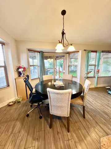 Wood-finish flooring throughout, bay window with blinds, sliding glass door with exterior access, and a ceiling-mounted chandelier