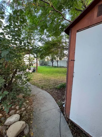 Expansive backyard featuring a lush lawn, mature trees, concrete pathway, and a detached shed