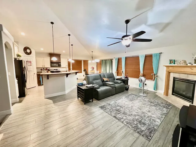 Open-concept living space featuring wood-finish flooring, a contemporary ceiling fan, and an integrated fireplace with a mantel