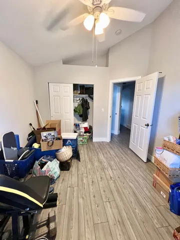 Wood-finish flooring throughout, vaulted ceiling with a ceiling fan, and a bi-fold closet with shelving