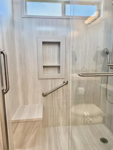 Walk-in shower with full-height stone-finish wall panels, built-in bench, recessed niche, and clear glass enclosure