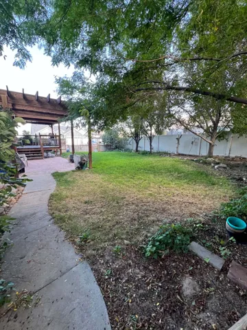 Expansive backyard featuring a wood pergola-covered deck, paver patio, concrete pathway, and mature trees