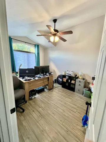 Sloped ceiling featuring a ceiling fan, a window with an arched top, and wood-finish flooring