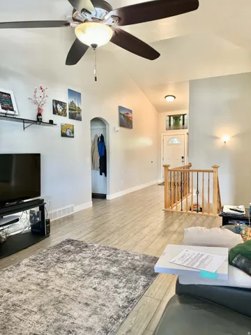 Vaulted ceiling with ceiling fan, wood-finish flooring, staircase with wood railing, arched doorway, and recessed lighting