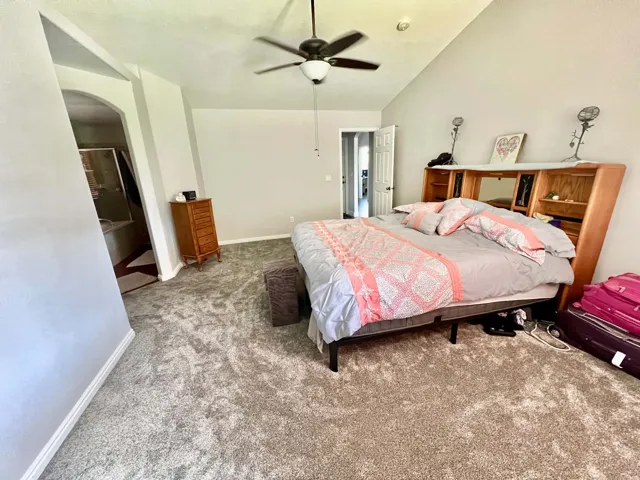 Vaulted ceiling with a ceiling fan, light gray wall paint, and gray carpet flooring