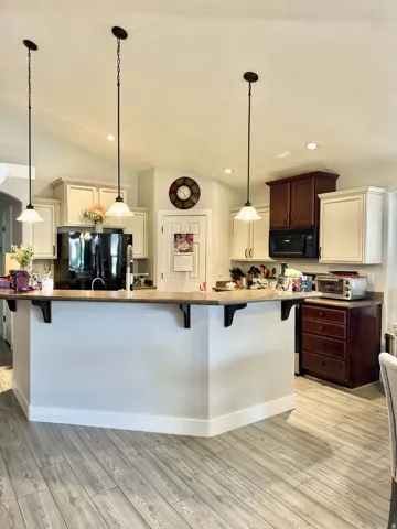 Vaulted ceiling with pendant lighting, kitchen island with seating, wood-finish flooring, and two-tone cabinetry