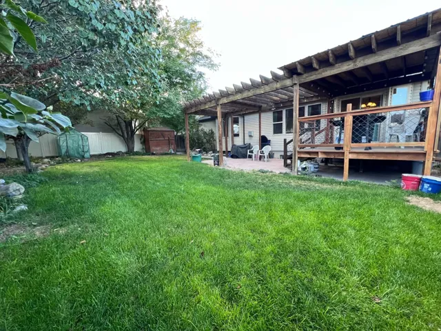 Expansive green lawn, elevated wood deck, wood pergola, and a paved patio area