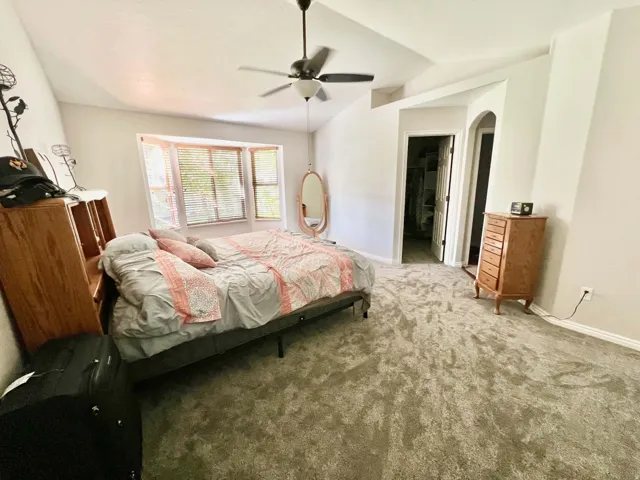 Vaulted ceilings with a ceiling fan, bay windows with blinds, and light-toned carpeting