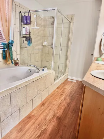Wood-finish flooring with a built-in tub and tiled surround, complemented by a glass-enclosed shower and a vanity with an integrated sink