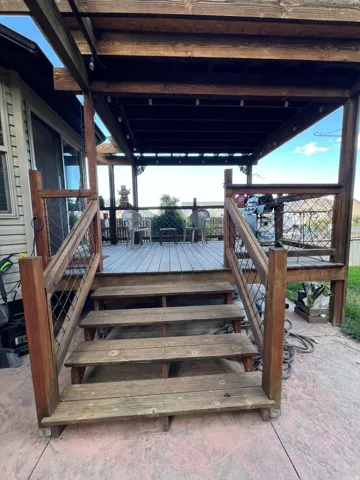 Multi-level wood deck featuring a covered pergola, exterior string lighting, and wood railing with metal infill