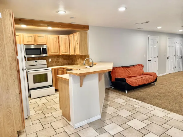 Kitchenette with wood-finish cabinetry, stainless steel appliances, tile backsplash, and a breakfast bar
