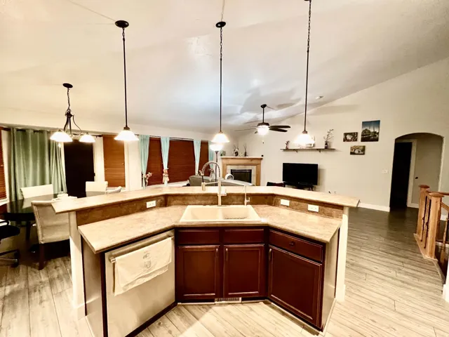 Kitchen island with integrated sink, vaulted ceiling, recessed lighting, wood-finish flooring, and a fireplace with wood mantel