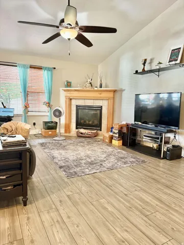 Vaulted ceiling with a ceiling fan, fireplace with a wood mantel and tile surround, and wood-finish flooring