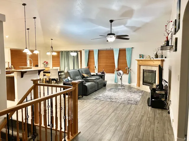 Vaulted ceilings with a ceiling fan, wood-finish flooring, a fireplace with a wood mantle, and a kitchen island with pendant lighting