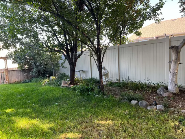 Expansive backyard featuring a manicured lawn, established trees, and a privacy fence