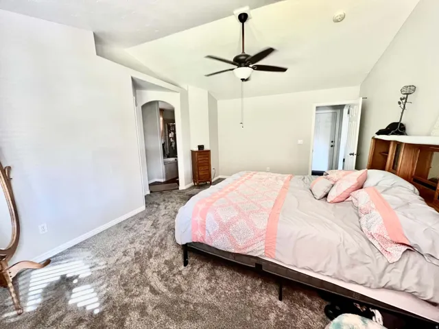 Vaulted ceiling with a ceiling fan, arched doorway, and soft gray carpeting