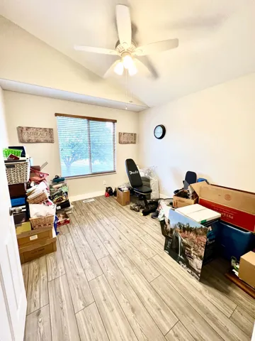 Vaulted ceiling featuring a ceiling fan with integrated lighting, wood-finish flooring, and window with blinds