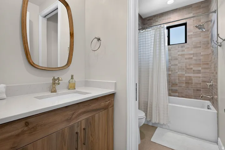 Bathroom featuring a wood-finish vanity with integrated sink, quartz-style countertop, and a shower-over-tub combination with tiled surround