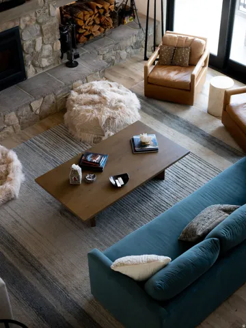 Stone fireplace featuring a hearth, wood-finish flooring, and a large area rug