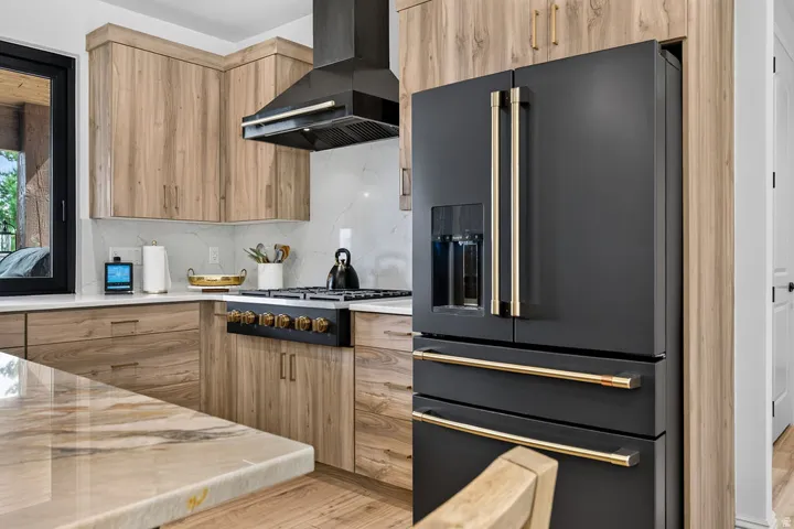Contemporary kitchen featuring light wood-finish cabinetry, white countertops, and a black range with gold-finish hardware