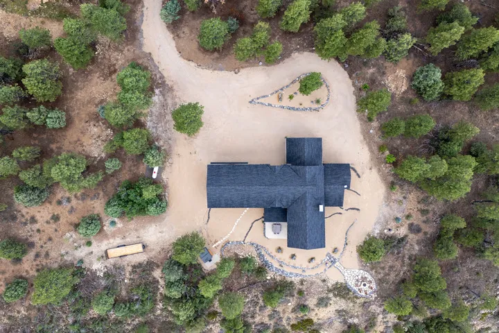 Dark shingle roof, gravel landscaping, stone fire pit area, and surrounding natural vegetation