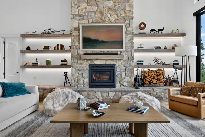 Stone-clad fireplace with a built-in firebox, flanked by custom floating shelves with integrated lighting, and a large picture window