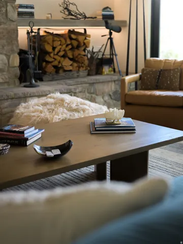 Stone-clad fireplace with a raised hearth, wood-finish mantel, and built-in wood storage