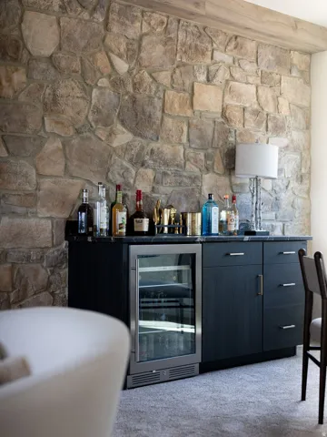 Stone accent wall, built-in cabinetry, integrated beverage refrigerator, dark countertop, and light-toned flooring