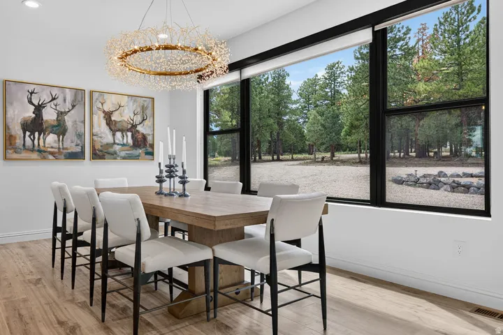 Expansive windows with black framing, wood-finish flooring, recessed lighting, and a prominent chandelier