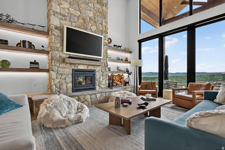 Floor-to-ceiling windows, stone fireplace with hearth, built-in recessed shelving with integrated lighting, wood-finish ceiling, and expansive outdoor scenery