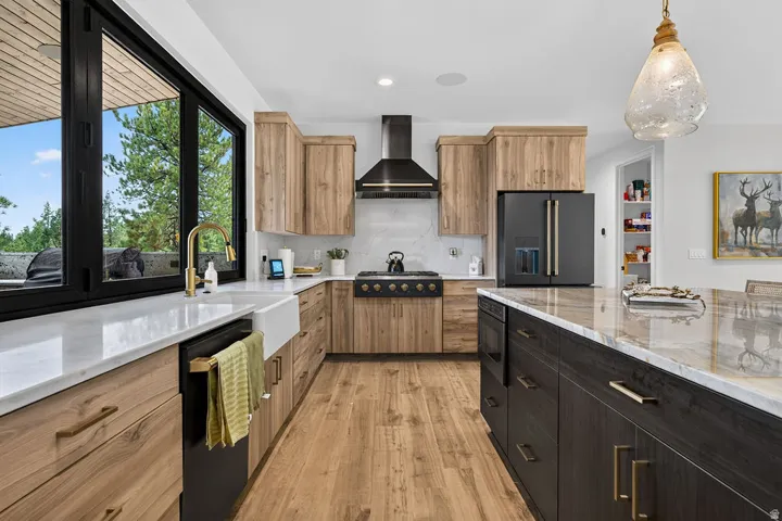 Gourmet kitchen featuring a large central island with integrated storage, wood-finish flooring, a farmhouse-style sink with a gold-tone faucet, and custom cabinetry
