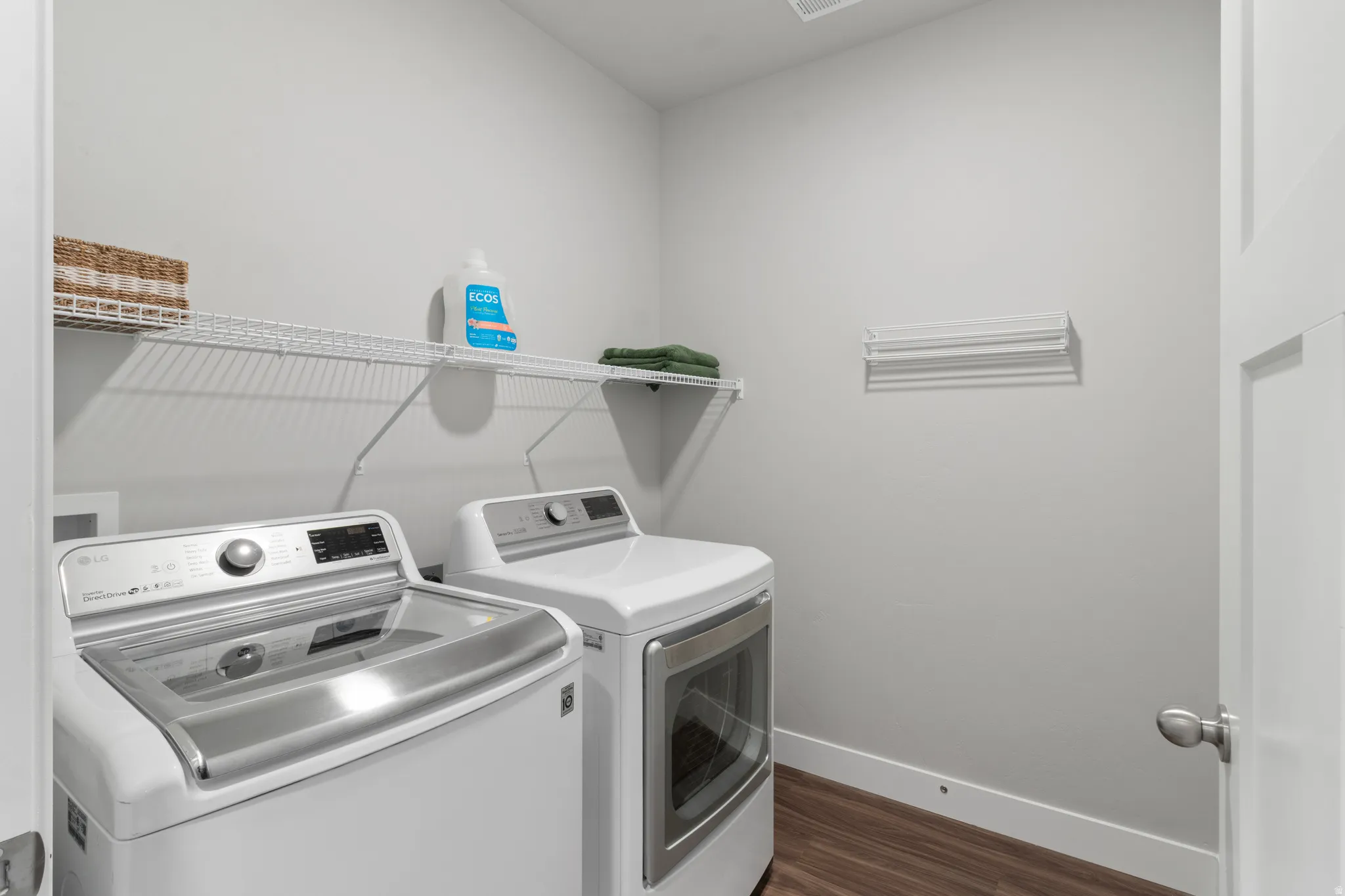 Laundry area featuring wood-finish flooring, white walls, and a white wire shelf