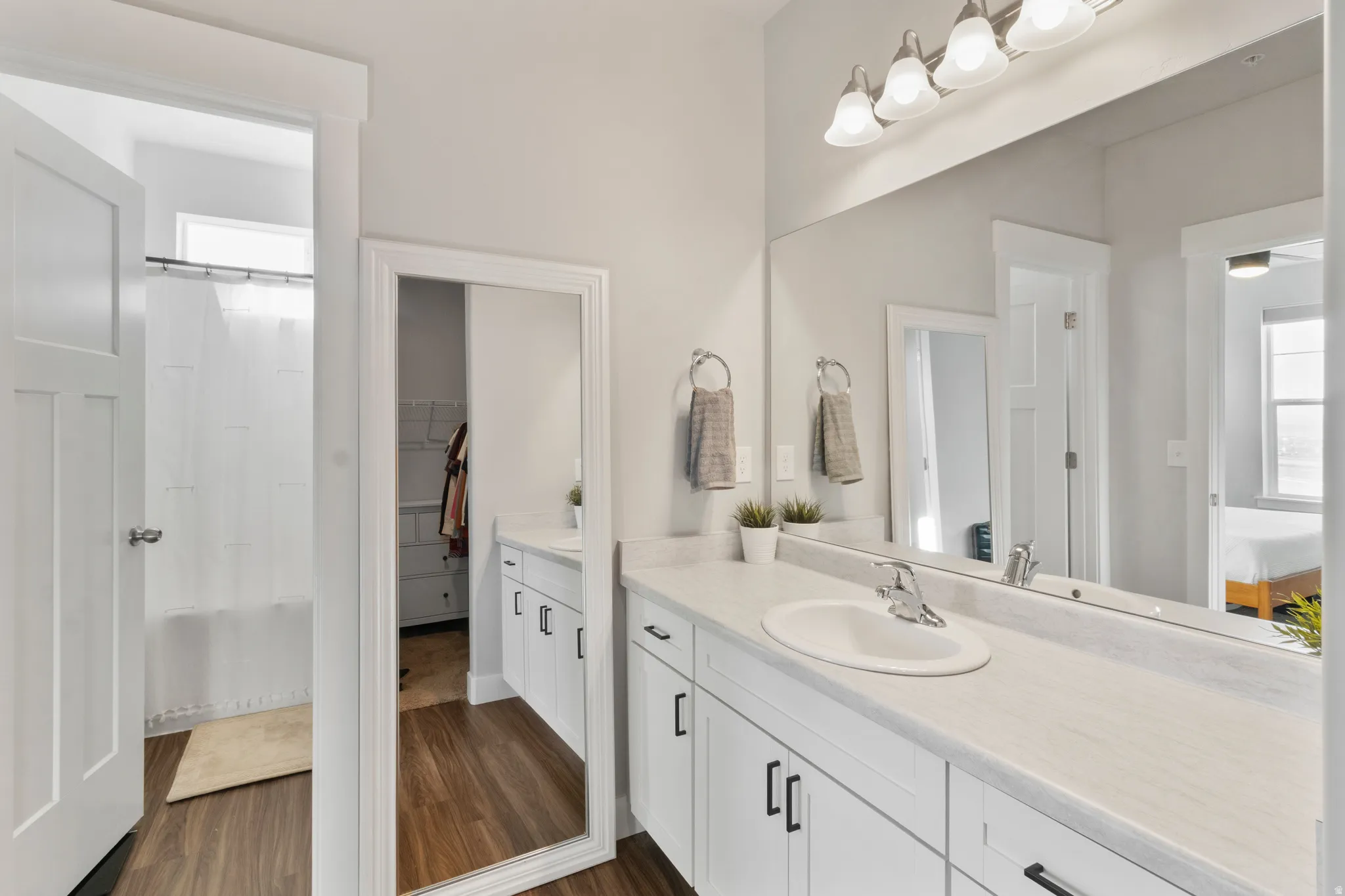 Dual vanity with white cabinetry, wood-finish flooring, and a large wall-mounted mirror