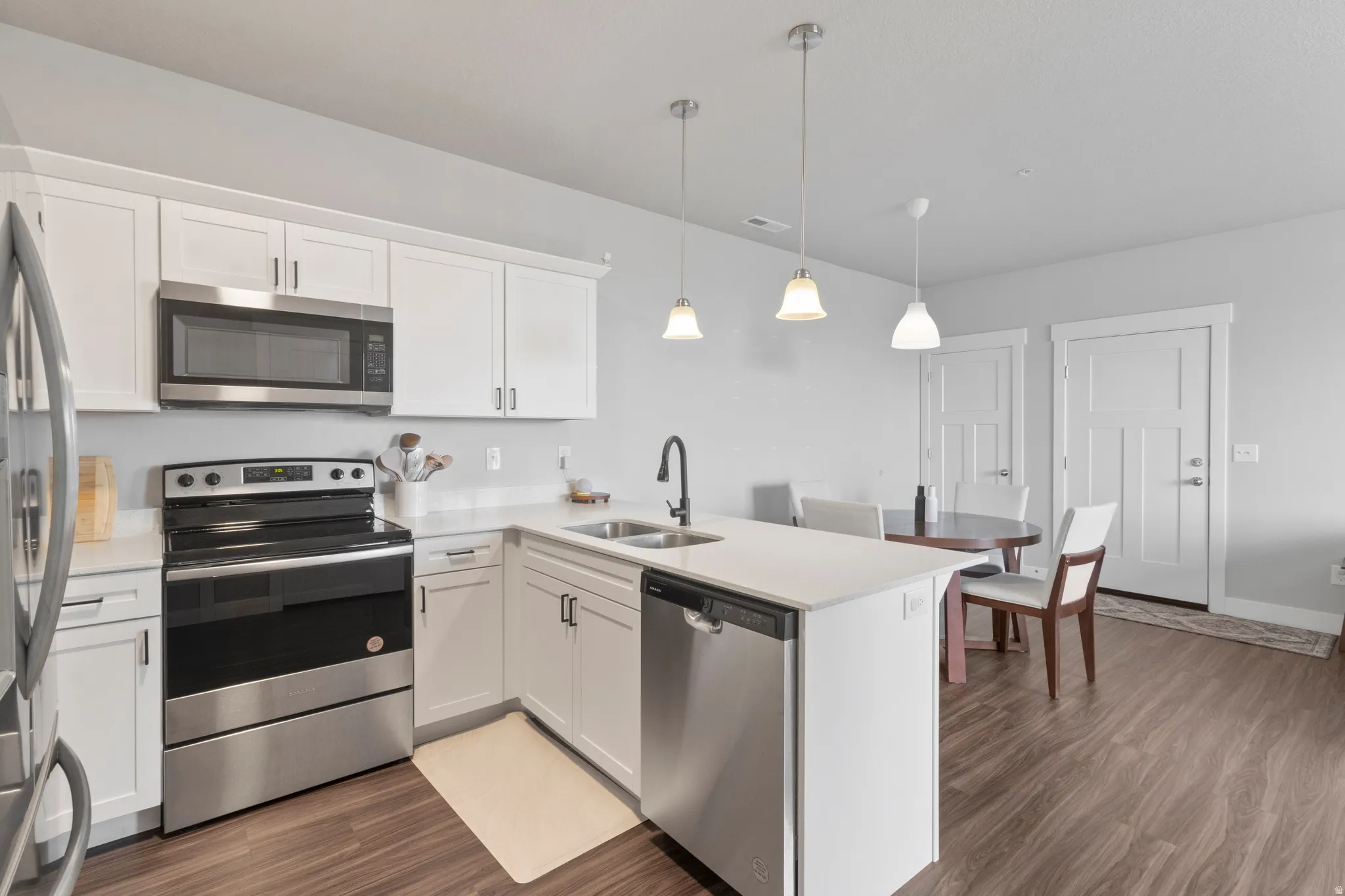 Kitchen featuring white cabinetry, stainless steel appliances, a kitchen island with sink, pendant lighting, and wood-finish flooring