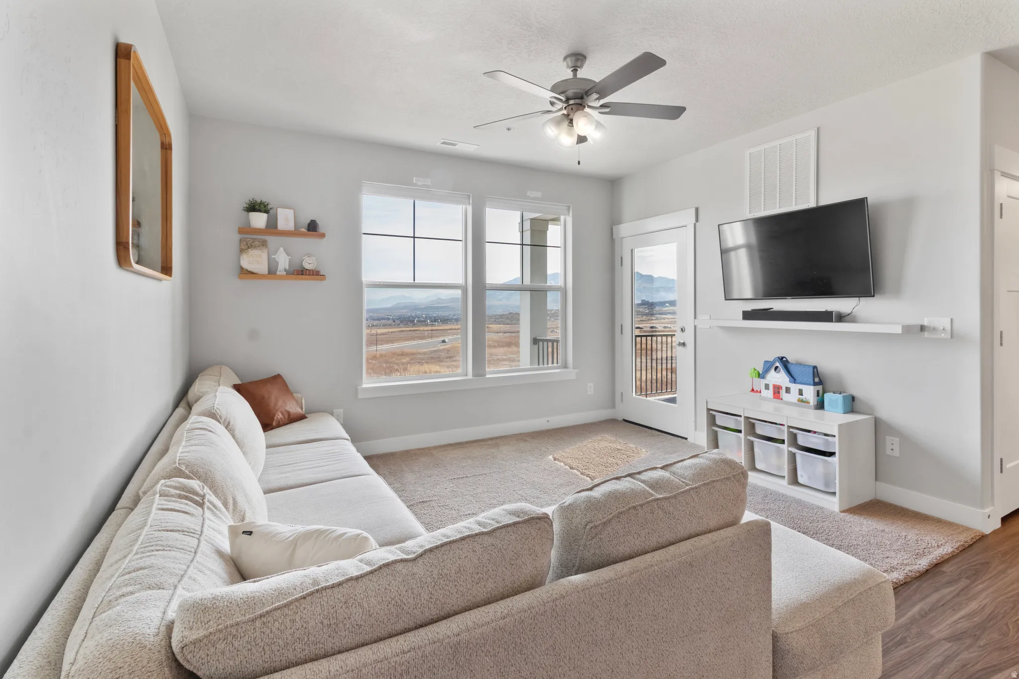 Bright living area featuring large windows, a glass-paneled door, and a ceiling fan