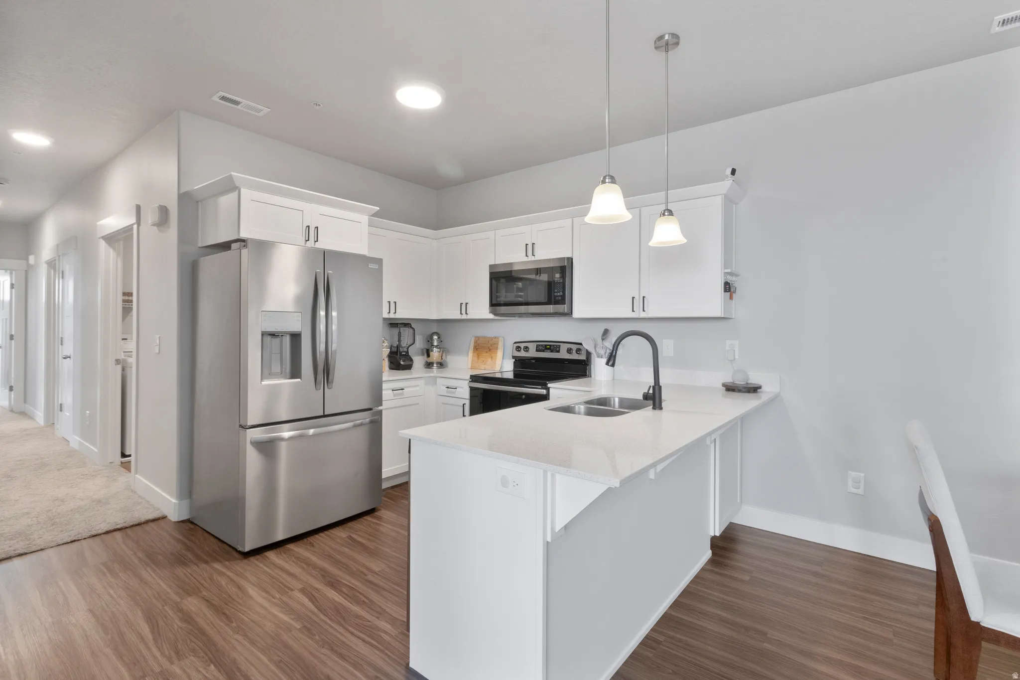 Kitchen featuring white shaker cabinetry, stainless steel appliances, wood-finish flooring, and a center island with pendant lighting