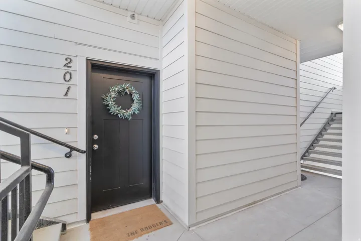 White horizontal siding exterior with a black entry door, featuring a white tongue-and-groove ceiling and a concrete walkway