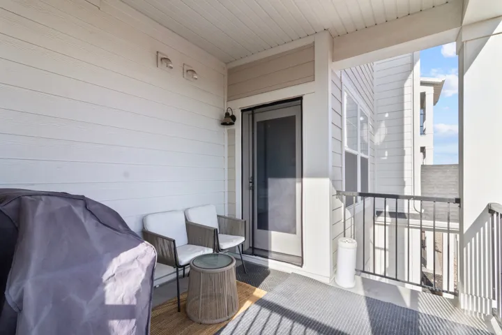 Covered outdoor balcony featuring a sliding glass door, overhead lighting fixture, and a black metal railing