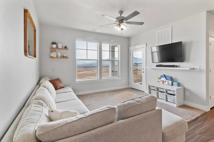 Bright living area featuring large windows, a glass-paneled door, and a ceiling fan