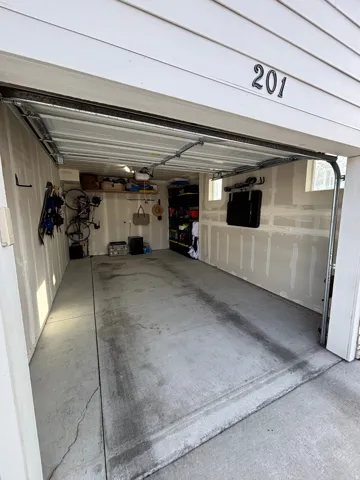 Attached single-car garage with concrete flooring, overhead storage shelving, and exposed wall framing