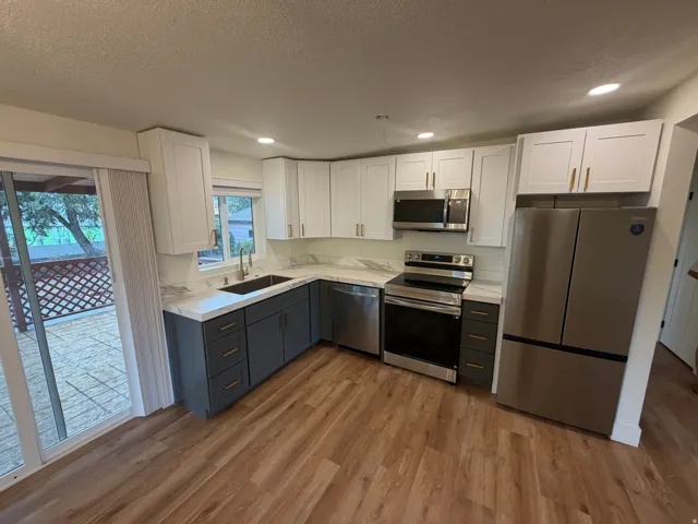 Modern kitchen featuring wood-finish flooring, two-tone cabinetry, stainless steel appliances, recessed lighting, and a sliding glass door to an outdoor patio