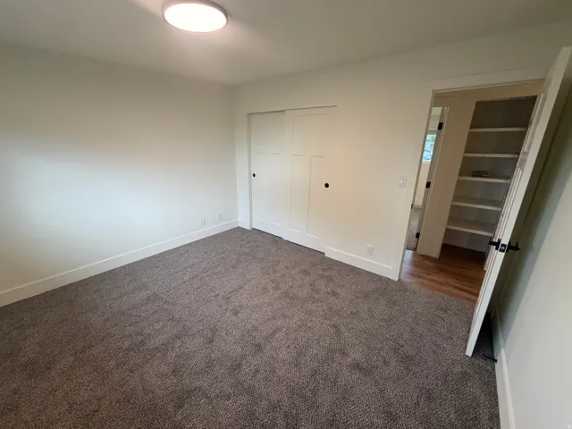 Plush carpet flooring, ceiling-mounted light fixture, white interior walls, sliding panel closet doors, and built-in shelving