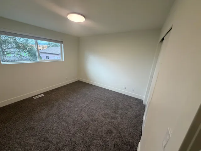 Bright secondary bedroom featuring expansive carpet flooring, recessed ceiling lighting, and a high transom window allowing abundant natural light