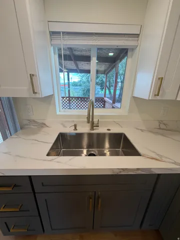 Stainless steel double basin sink with a gooseneck faucet, set into a white countertop with gray veining