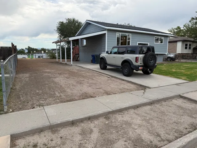 Exterior featuring gray siding, a covered carport, and a chain-link fence